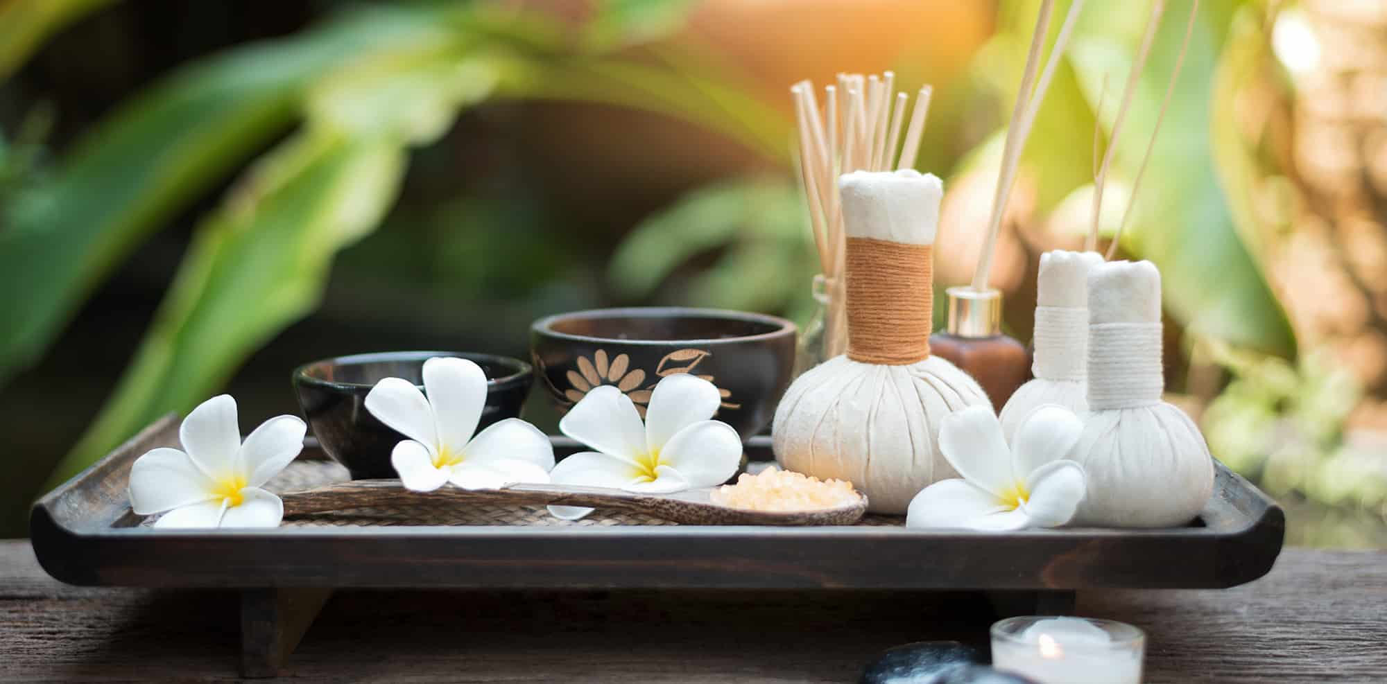 Plumeria-Blüten, Kräuterstempel und Räucherstäbchen auf einem Holztablett